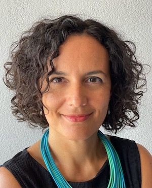 Person with curly dark hair wearing a black tank top and a turquoise necklace.