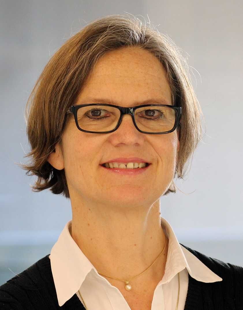 Person wearing a white collared shirt, black sweater, and gold necklace with a pearl pendant.